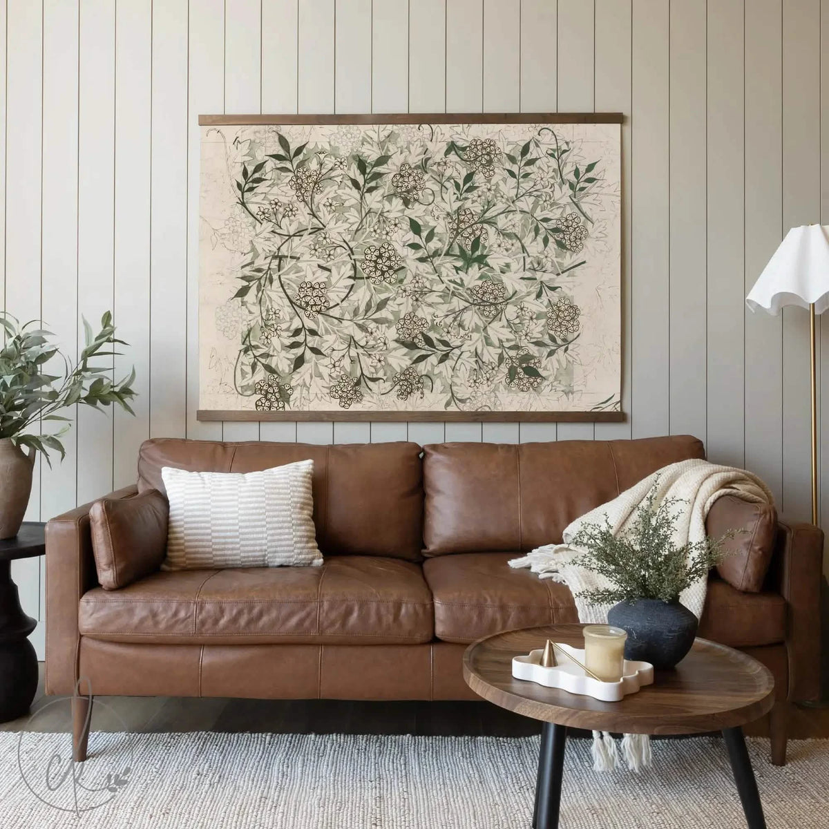 Large vintage botanical wall art featuring an intricate floral design in earthy tones, elegantly displayed above a brown leather sofa in a cozy living room with neutral decor. William Morris