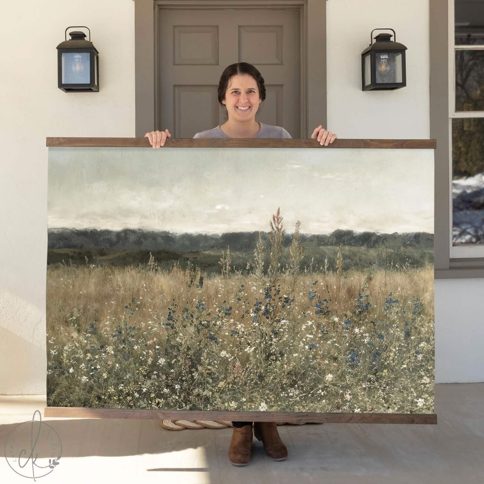 Person holding a large framed artwork of a landscape with a field and sky.