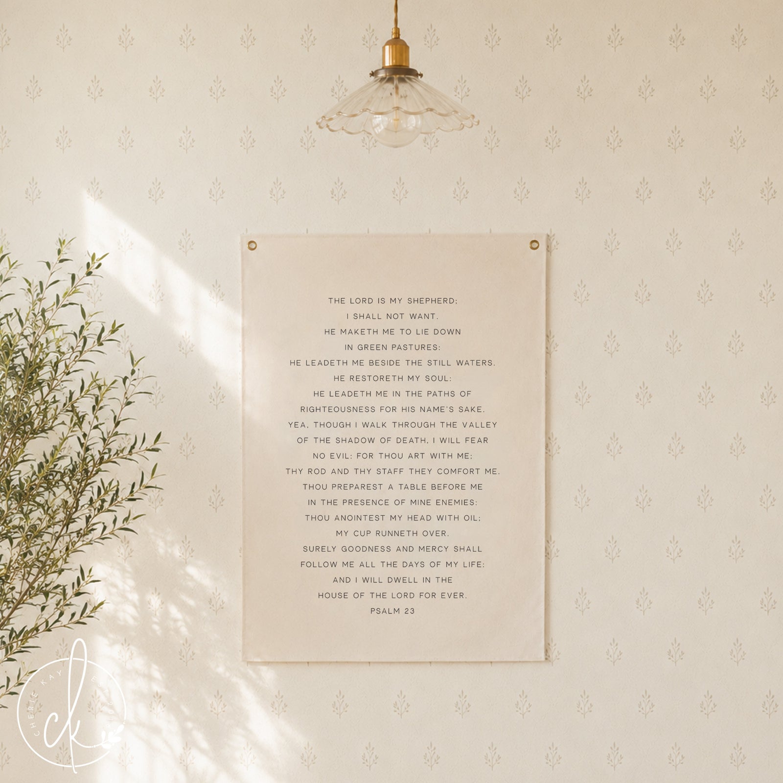 A beige canvas wall hanging with the text of Psalm 23 in black. The text is centered on the canvas, which is hung on a white wall. The canvas has two brass grommets at the top for hanging.