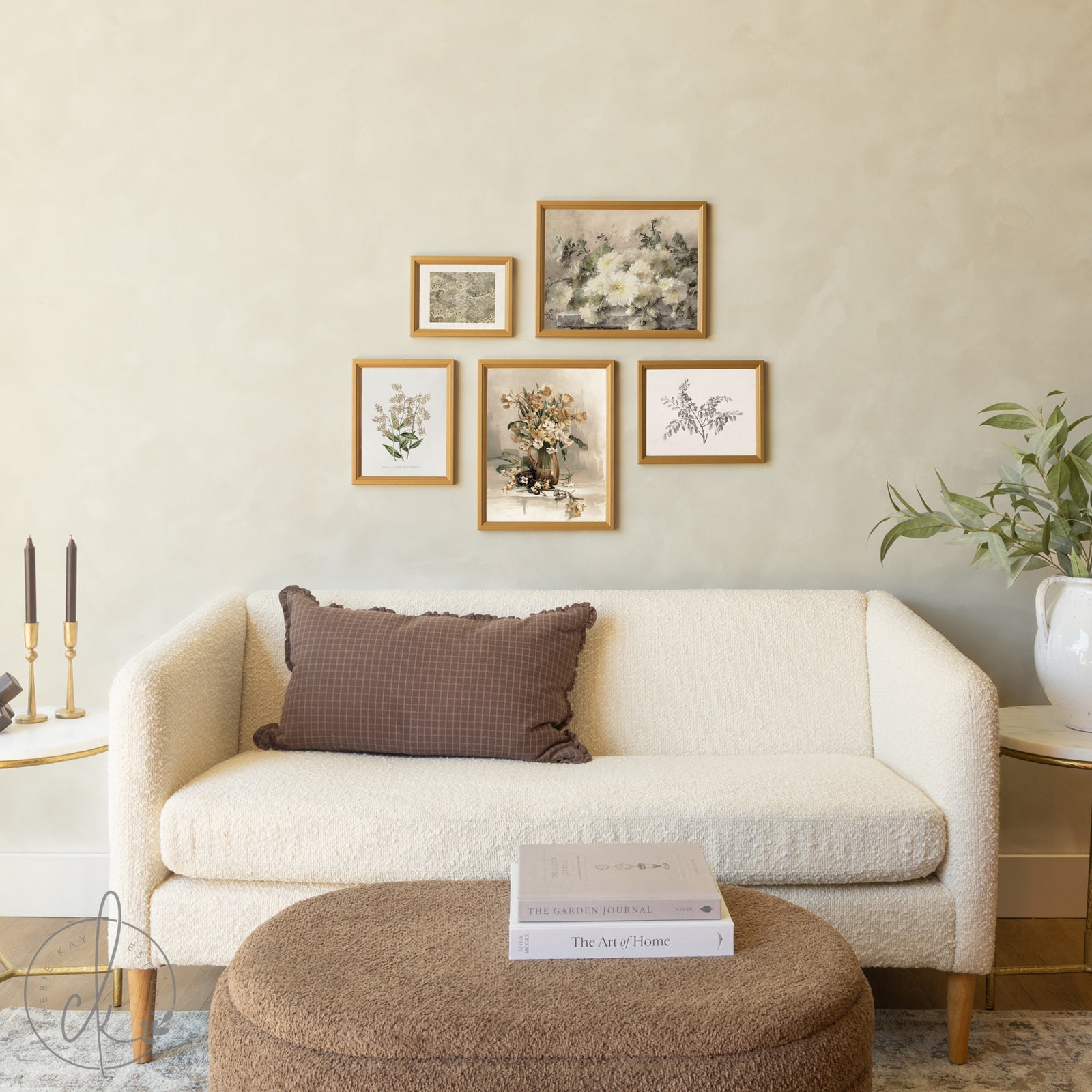 Five gold-framed botanical artworks arranged in a symmetrical diamond pattern above a cream boucle sofa, featuring vintage floral paintings, botanical illustrations, and nature prints, complemented by a round textured ottoman and modern decor elements.