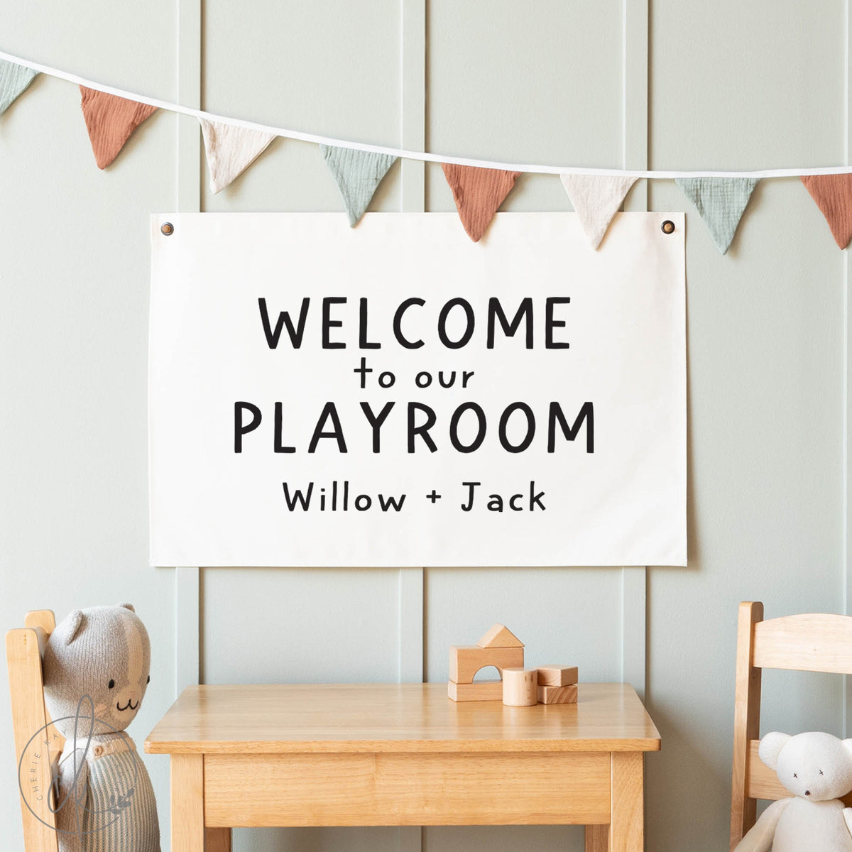 Playroom sign with &#39;Welcome to our Playroom Willow + Jack&#39; text, wooden table, and chairs with teddy bears.