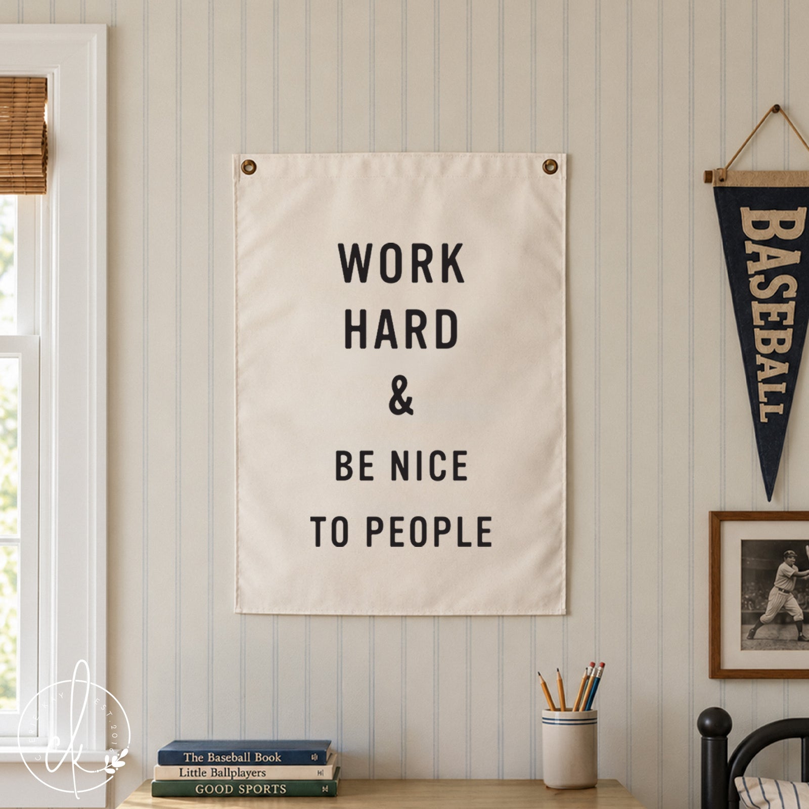 A white rectangular wall hanging featuring the black printed text WORK HARD & BE NICE TO PEOPLE. The sign is secured with two metal grommets at the top corners and displays a clean, bold sans-serif font against a plain white background.