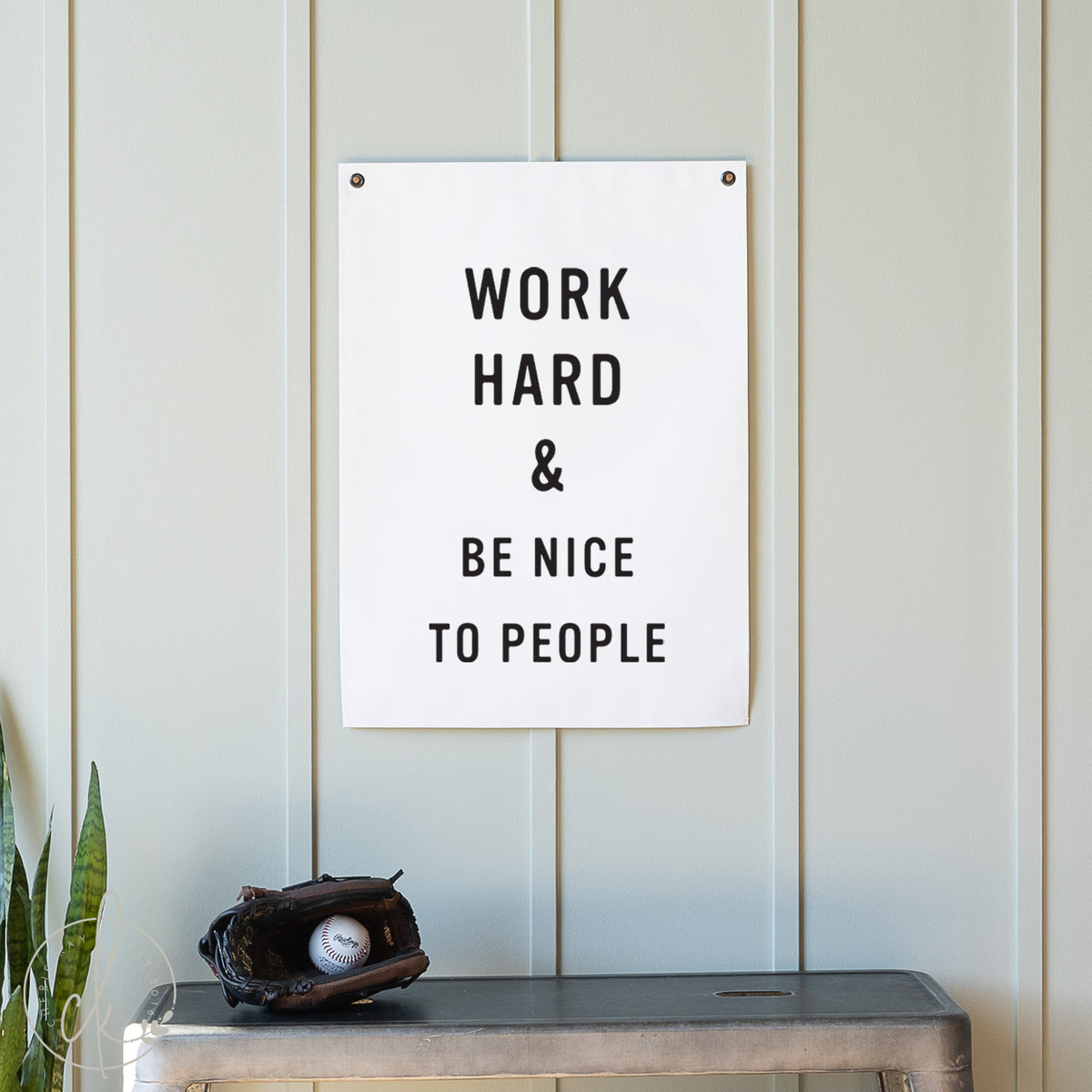 Motivational poster with &#39;Work Hard &amp; Be Nice To People&#39; text on a wall with a plant and baseball glove below.