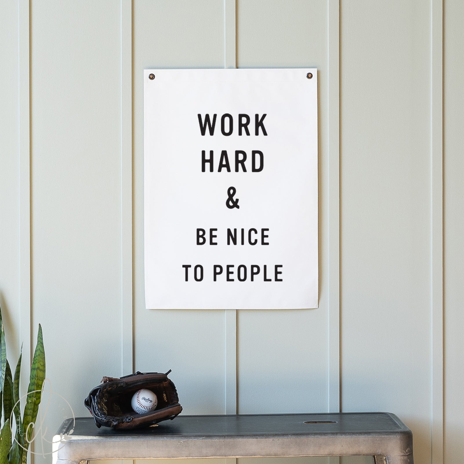 Motivational poster with 'Work Hard & Be Nice To People' text on a wall with a plant and baseball glove below.